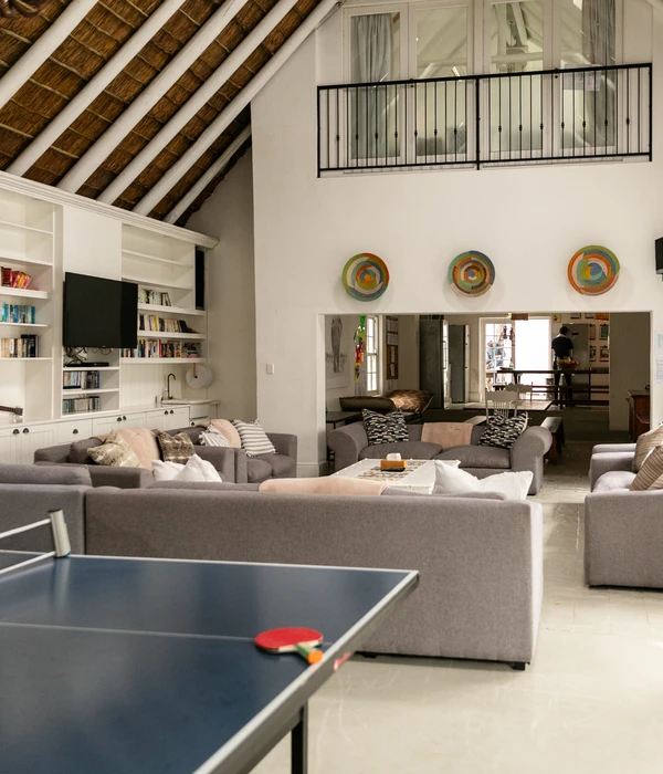Een gemeenschappelijke ruimte met een hoog plafond, meerdere banken, ingebouwde boekenkasten, een tv en een pingpongtafel op de voorgrond.