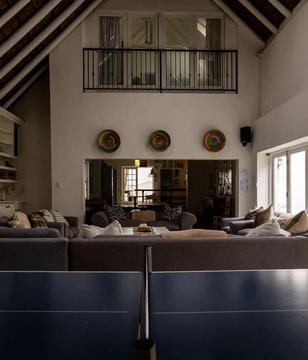 Ruime gemeenschappelijke lounge met grijze banken, een pingpongtafel op de voorgrond en een mezzaninebalkon onder een hoog plafond.